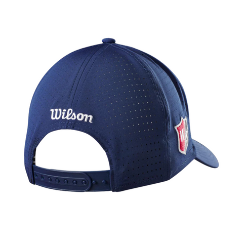 The Wilson Performance Mesh Cap is a navy blue adjustable hat with ventilation holes for breathability, featuring a white Wilson logo above the snapback and a red and white shield patch on the side.