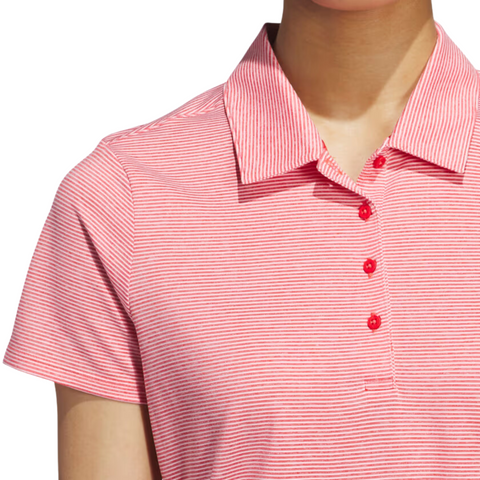 A person wears an Adidas Womens Ottoman Short Sleeve Polo Shirt, featuring thin pink and white stripes, a collar, and a four-button placket with red buttons; the persons head is partially out of frame.