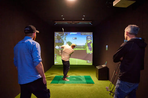 Two people looking on while a player hits a shot in the indoor golf studio at Golf 360