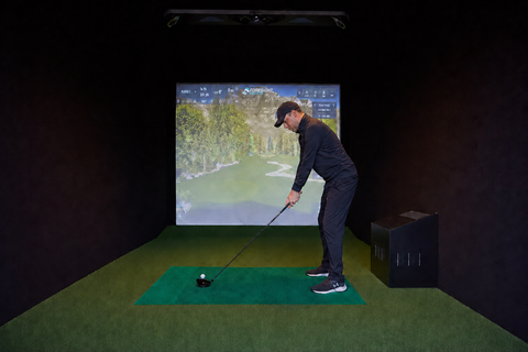 A left handed golfer in a golf simulator about to hit a driver