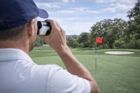 A male golfer aiming his rangefinder at a red golf flag 
