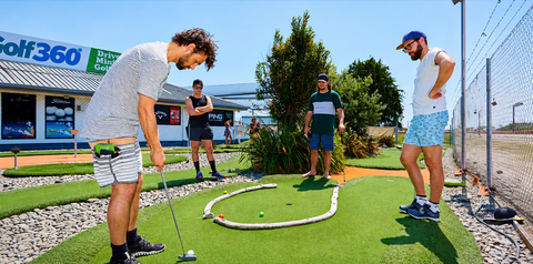 Four guys enjoying a game of mini golf at Golf 360.  Playing a challenging hole with a rope to navigate around