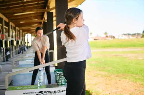 A young female having a hit on the driving range at Golf 360
