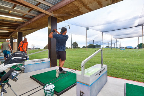 Golfer hitting an iron from a covered bay at Golf 360 driving range in Mount Maunganui, overlooking the grass range