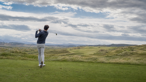 Right-handed golfer playing a controlled shot in strong wind