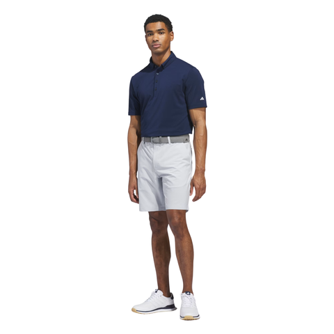 Men's Adidas golf polo in navy blue paired with light grey golf shorts and white golf shoes, designed for comfort, performance, and modern on-course style.