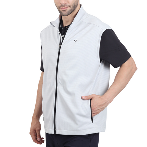 A man wearing a light gray zip-up vest over a black short-sleeve polo shirt, with one hand in the vest pocket, standing against a white background.