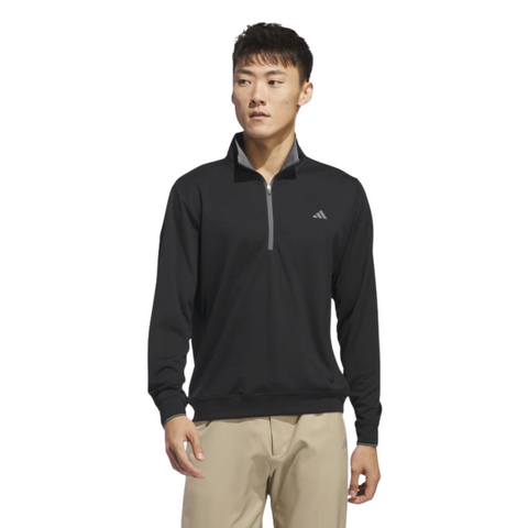 A man in beige pants models the Adidas Mens Core Lightweight Zip Top in black, standing sideways against a white background to showcase this lightweight, breathable outer layer.