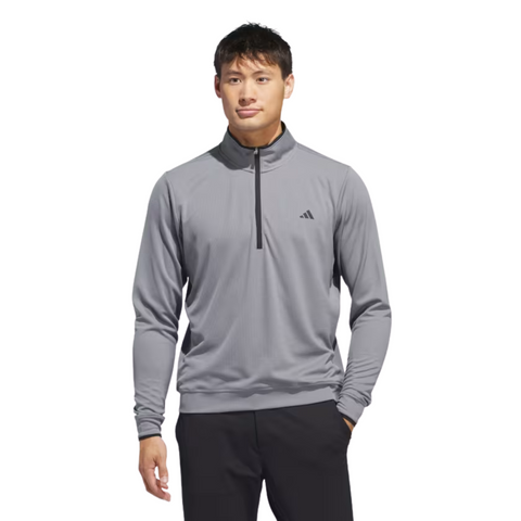 A man faces forward against a white background, wearing the Adidas Mens Core Lightweight Zip Top in light gray with a small black logo on the left chest, paired with black pants.
