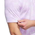 A person pinches the sleeve of an Adidas Men's Go-To Printed Polo Shirt in Powder Plum/White, highlighting the cotton-blend fabric texture and fit on their upper arm.