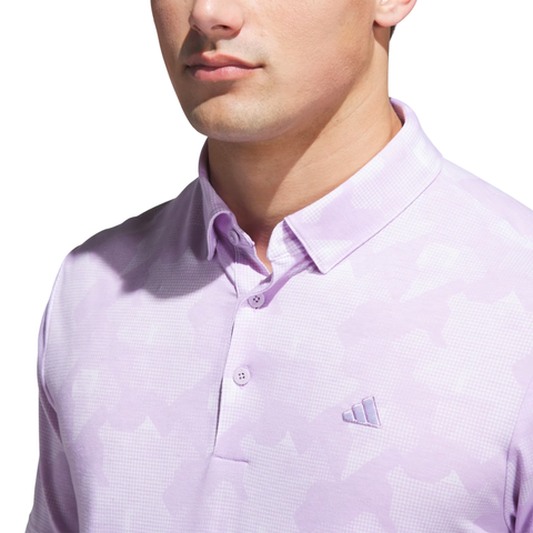 A man models the Adidas Men's Go-To Printed Polo Shirt in Powder Plum/White, featuring a subtle pattern and chest logo—an ideal men’s printed polo for golf—shown from the shoulders up against a white background.
