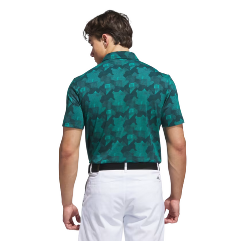 A man faces away in an Adidas Mens Go-To Printed Polo Shirt (Pure Teal/Ivy), featuring lightweight performance fabric, paired with white pants and a black belt, standing against a white background.