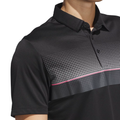A person wears the Adidas Men's Performance Allover Print Polo Shirt in black, featuring a black collar, gradient white dots, and a horizontal pink stripe. The cropped image highlights only the upper torso and neck.