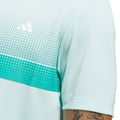 A close-up of an Adidas Mens Performance Chest Stripe Print Polo Shirt in Flash Aqua, showing green and white dotted stripes and logo. A tattooed arm is partially visible. Moisture-wicking fabric keeps you comfortable on the course.