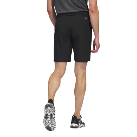 A man in a dark shirt and Adidas Men's Ultimate365 8.5" Golf Shorts with black athletic shoes featuring white soles is seen from behind, highlighting the stretch comfort of his Adidas outfit.