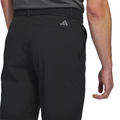 A person is seen from the lower back and arm, wearing black Adidas Men's Ultimate365 8.5" Golf Shorts with a woven black belt and a gray shirt. The shorts display a small Adidas logo above the back pocket.