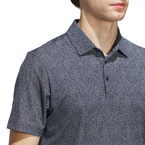 A man wears the Adidas Mens Ultimate365 Bunker Polo Shirt in Collegiate Navy, a short-sleeved, collared, patterned design, shown from shoulders to mid-torso against a white background.
