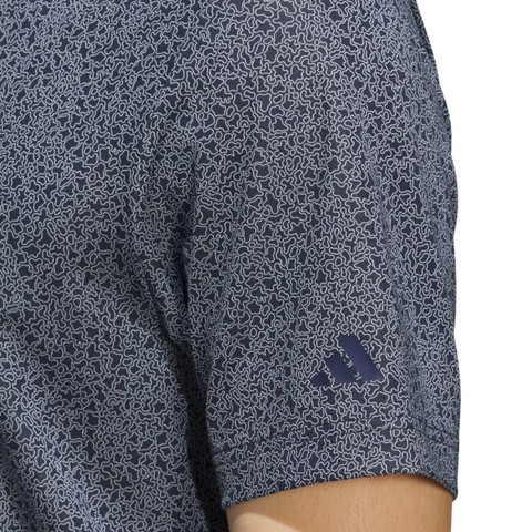 Close-up of a person’s upper arm wearing the Adidas Men’s Ultimate365 Bunker Polo Shirt in collegiate navy, showing a light squiggly pattern and a small blue Adidas logo near the sleeve hem.