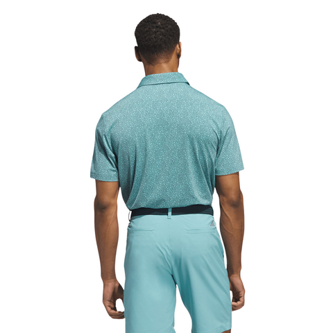 A man faces away in a Pure Teal Adidas Mens Ultimate365 Bunker Polo Shirt, paired with light blue shorts. His relaxed stance spotlights this stylish Adidas golf polo against a white background.