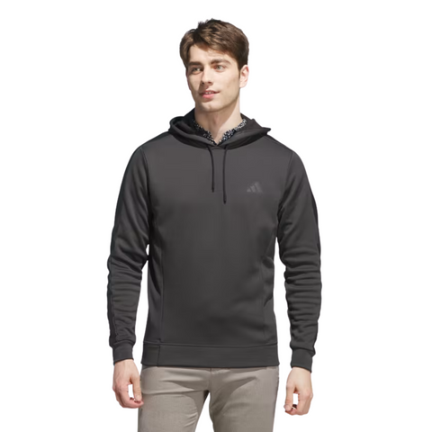 A man stands against a white background, wearing an Adidas Men's Ultimate365 Hoodie in Grey/Black with a small chest logo, layered over a collared shirt and paired with light-colored pants.