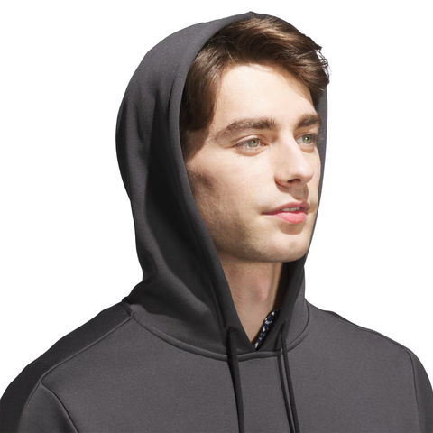 A young man with light skin and brown hair wears the Adidas Mens Ultimate365 Hoodie in dark gray, featuring four-way stretch fleece, hood up, looking slightly right against a plain white background.