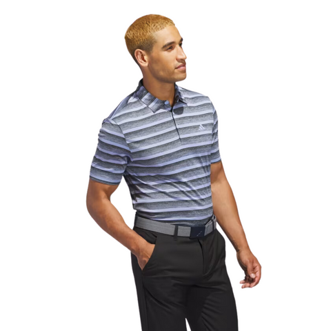 A man with short blonde hair models the Adidas Two-Colour Striped Men's Polo Shirt in blue, gray, and white stripes with black pants, standing against a white background and looking to the side.