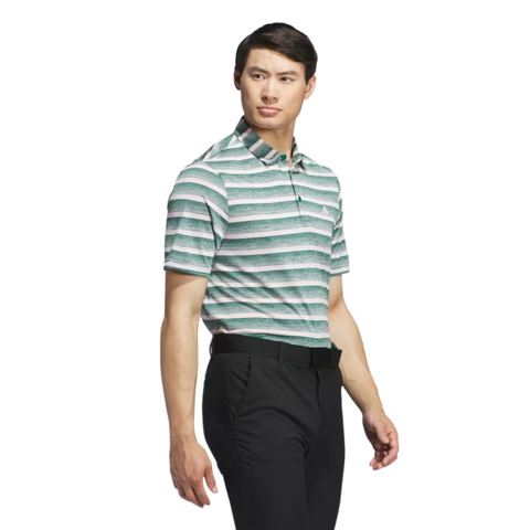 A man wearing an Adidas Two-Colour Striped Men's Polo Shirt in green and white stripes with black pants stands slightly turned to the side against a white background.