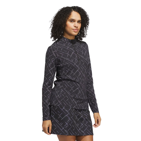 A woman with curly hair wears the Adidas Ultimate365 Printed Quarter-Zip Long-Sleeve Polo Shirt in Black/Powder Plum, standing at an angle against a plain white background.