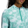 A person wearing an Adidas Ultimate365 Printed Quarter-Zip Long-Sleeve Polo Shirt in Pure Teal, shown from shoulders to mouth. The quarter-zip is closed, long curly hair is partially visible, and the background is plain white.