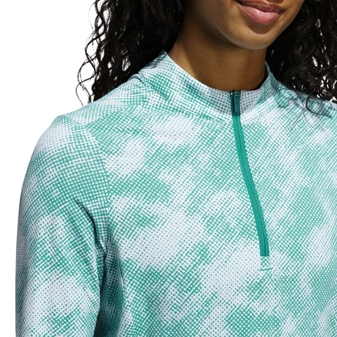 A person wearing an Adidas Ultimate365 Printed Quarter-Zip Long-Sleeve Polo Shirt in Pure Teal, shown from shoulders to mouth. The quarter-zip is closed, long curly hair is partially visible, and the background is plain white.