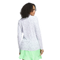A woman with curly hair wears the Adidas Ultimate365 Printed Quarter-Zip Long-Sleeve Polo Shirt in white, paired with a light green ruffled skirt. She stands facing away from the camera.