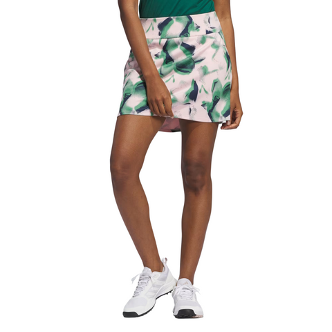 A person in a green top, white sneakers, and an Adidas Ultimate365 Women's Skort by Adidas with a green leaf pattern stands against a white background, one leg slightly forward.