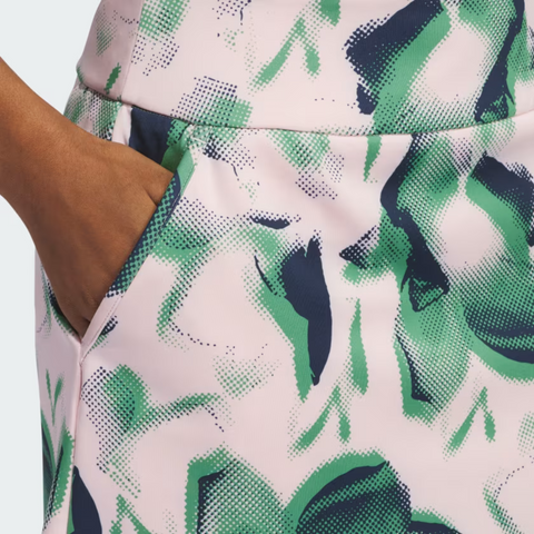Close-up of a medium-brown hand in the pocket of an Adidas Ultimate365 Women's Skort by Adidas, featuring an abstract green, navy, and light pink pattern.
