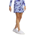 A woman wears the Adidas Ultimate365 Women's Skort in a blue and purple floral print with a matching long-sleeve Adidas top and white sneakers, shown from shoulders to feet on a white background.