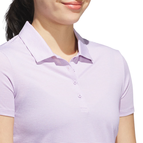 A woman models the Adidas Women’s Ottoman Short Sleeve Polo Shirt in Powder Plum, featuring short sleeves and a collar, shown from shoulders to chin against a white background.