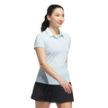 A woman with long dark hair in a ponytail wears the Adidas Womens Ottoman Short Sleeve Polo Shirt in light blue and a black skirt, smiling as she walks forward against a white background. This moisture-wicking polo keeps her cool and comfortable.