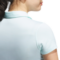 A close-up shows a woman from behind with her upper back, neck, and part of her face visible. She wears a light blue Adidas Womens Ottoman Short Sleeve Polo Shirt and has dark hair tied back.