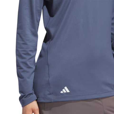 A person is shown from the torso wearing an Adidas Women's Performance Golf Hoodie in blue, featuring long sleeves, soft stretch fabric, and the Adidas logo near the waist, paired with brown pants.