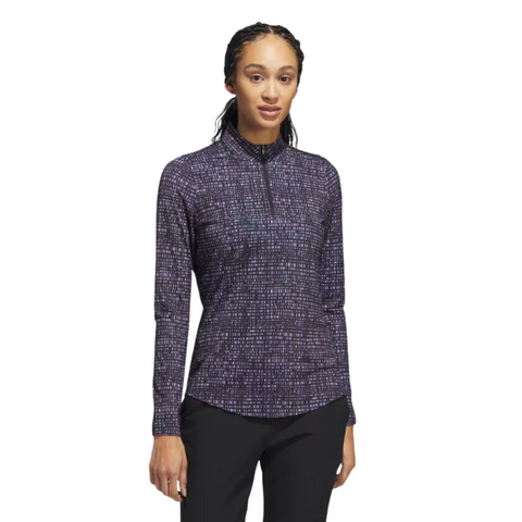 The Adidas Ultimate365 Women's Long Sleeve Golf Shirt in Black Noir, worn by a model, features a grid-like abstract pattern in purple, blue, and white on a black background, with a zippered collar and long sleeves.