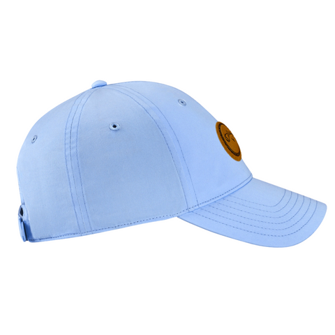 The Callaway Women’s Heritage Twill Golf Cap features light blue twill, a round brown front patch, visible stitching, and an adjustable back. Designed for sun protection, it’s shown from the side on a white background.