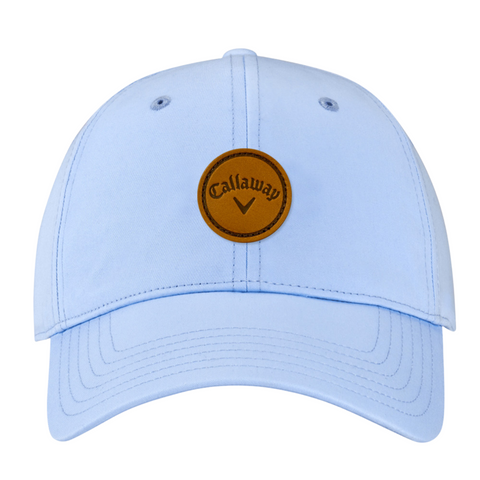 The Callaway Women’s Heritage Twill Golf Cap in light blue features a brown circular leather patch with the Callaway name and black chevron logo, plus an adjustable fit for stylish sun protection.