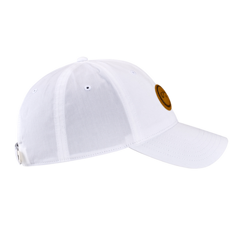 The Callaway Women’s Heritage Twill Golf Cap, shown in white with a curved brim, features a brown circular front patch, ventilation eyelets, and an adjustable back strap for fit.
