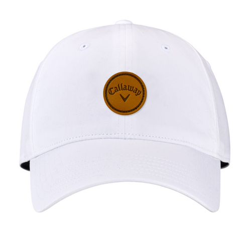 The Callaway Women’s Heritage Twill Golf Cap is white with a round brown leather patch, displaying the black Callaway logo and chevron. It features sun protection and an adjustable fit for comfort on the course.
