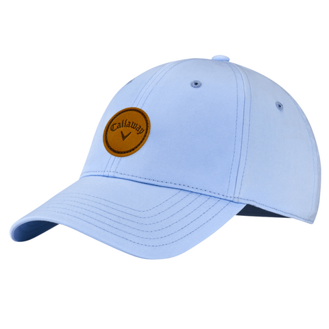 The Callaway Women’s Heritage Twill Golf Cap features a light blue design, curved brim, brown circular logo patch on the front, and an adjustable fit for comfort and UV sun protection.