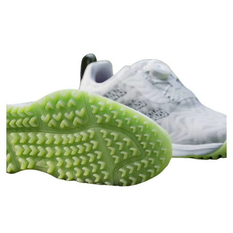 Close-up of the Adidas Codechaos BOA junior golf shoes, showcasing the lime green spikeless outsole with a textured pattern for enhanced grip. The shoes have a white upper with black details, and a heel pull tab for easy wear.