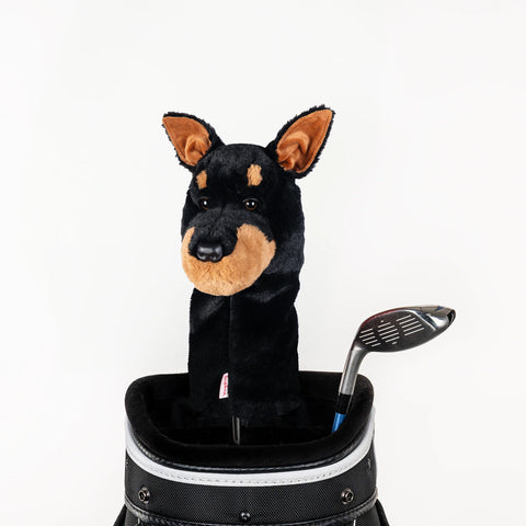 A golf bag displays a club with a Daphnes Animal Golf Headcover by Daphne, shaped like a black and brown Doberman dog, beside an uncovered club on a white background—ideal for fans of animal-themed golf accessories.