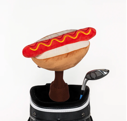 A Daphnes Animal Golf Headcover shaped like a plush hot dog with mustard and ketchup details rests next to a golf club and bag against a white background. Ideal for fans of fun or Daphnes unique golf accessories.