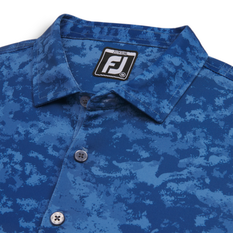 Close-up of the FootJoy Boys' Cloud Camo Polo, highlighting the blue cloud camouflage pattern, three-button placket, and branded collar tag. Made from performance fabric for comfort and mobility.