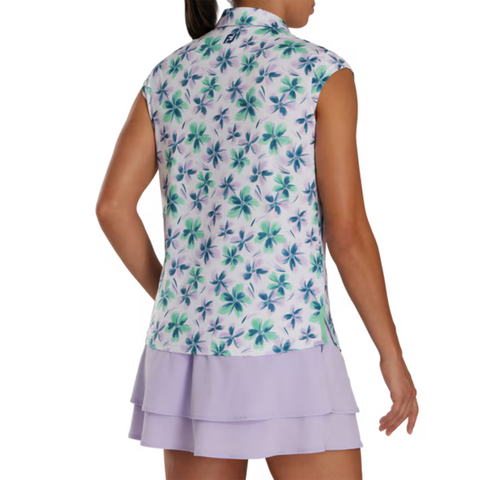 Back view of a model wearing a sleeveless floral golf top by FootJoy, featuring a green and blue floral pattern on a white base. Paired with a light lavender pleated golf skirt.