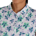Close-up front view of a model wearing a sleeveless floral golf top by FootJoy. The shirt features a white background with a green and blue floral pattern, buttoned down with a collar.